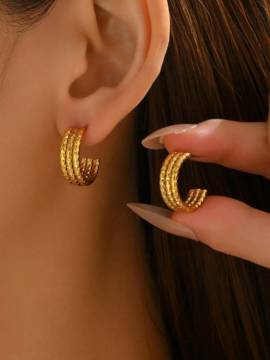 Close-up of a woman wearing 18K gold-plated textured triple band hoop earrings. The earrings feature a layered, textured finish with a radiant gold shine, styled with manicured nails gently adjusting one hoop